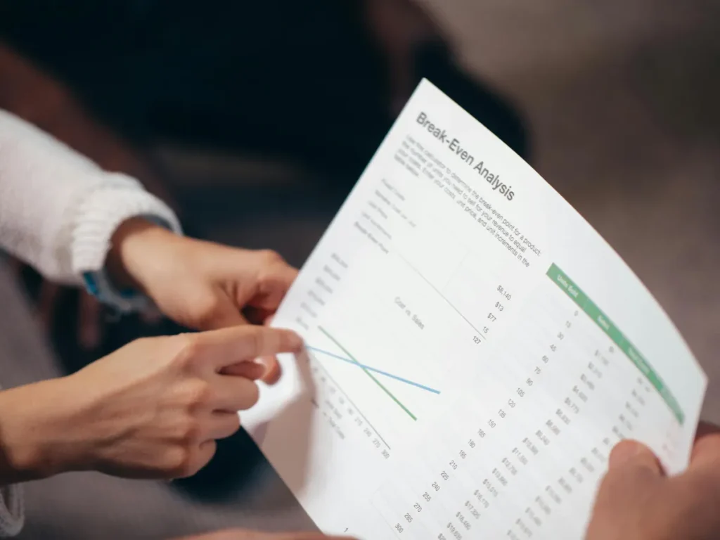 Tangan mendiskusikan dokumen analisis break even point dengan grafik biaya dan pendapatan